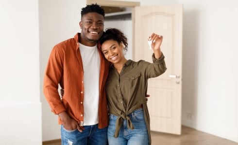 Homebuying as an Unmarried Couple: What to Consider. Real Estate. Cheerful African American Spouses Showing New House Key Smiling To Camera, Embracing Standing Among Moving Cardboard Boxes At Home. Relocation, Apartment Ownership And Family Housing